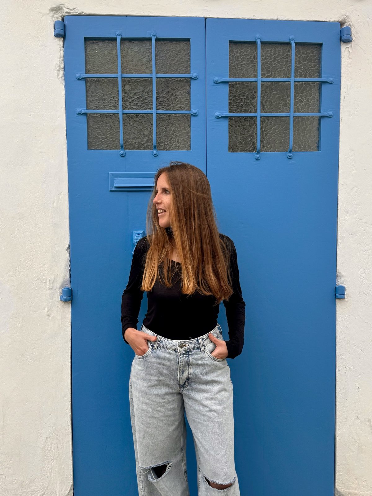 Andrea Casal, con camiseta negra y vaqueros, sonriendo delante de una puerta azul